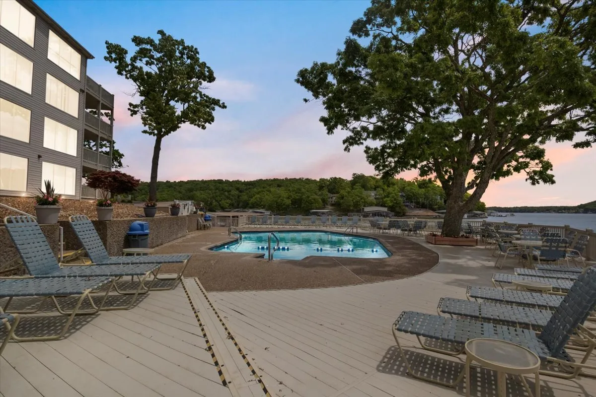 A serene outdoor pool area with lounge chairs, surrounded by trees and offering glimpses of the lake. The space is tranquil and designed for relaxation, swimming, or socializing, with the water adding to the sense of calm.