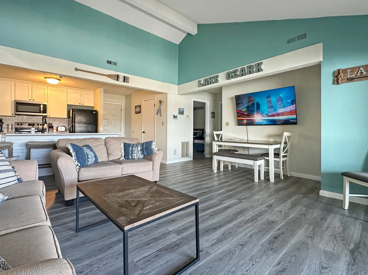 A spacious, inviting open-concept living area featuring a comfortable sofa, coffee table, TV, dining table, and a modern kitchen. The room is bright and thoughtfully arranged, ideal for relaxation, socializing, or casual meals.