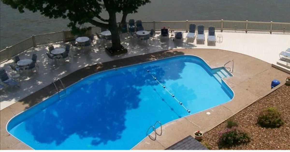 This image showcases a sparkling swimming pool surrounded by loungers and a tree that provides natural shade. The pool area is tranquil and inviting, suggesting a perfect spot for family fun, swimming, and poolside relaxation. The presence of seating encourages social interaction and relaxation after activities.
