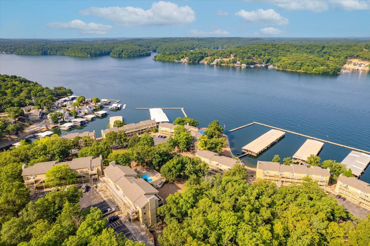 This image captures the lake, marina with docks, surrounding trees, and nearby buildings. The scene is peaceful and vibrant, showing the proximity of the condo to the main water activities area. People can be imagined swimming, boating, or picnicking along the water's edge.