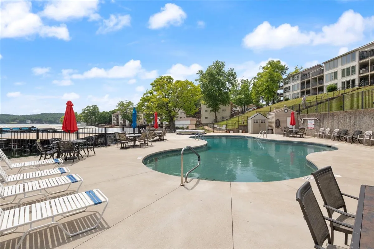 A vibrant exterior shot of the swimming pool surrounded by lounge chairs, umbrellas, lush greenery, and the scenic waterfront. The inviting pool area suggests socializing, relaxing, and barbecuing—key activities for groups of friends.
