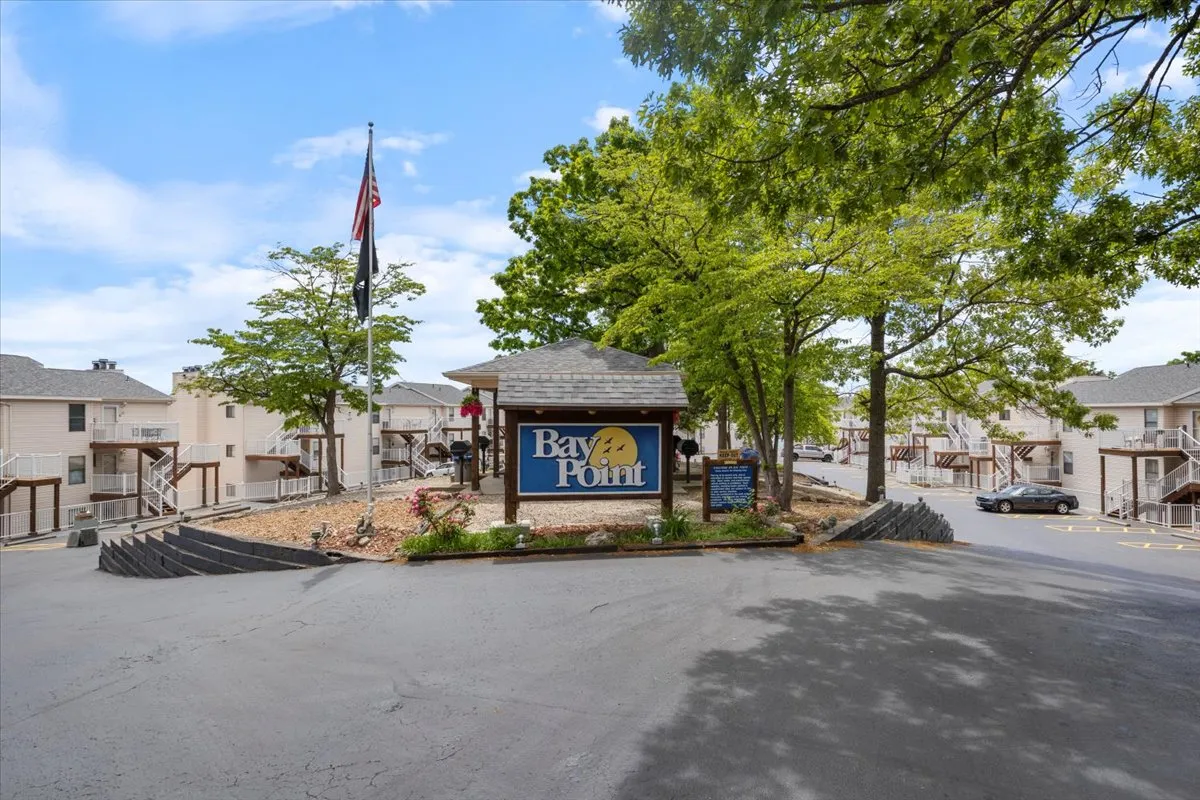 A welcoming exterior shot showing the main entrance sign of the property, surrounded by mature trees and a parking area, bathed in sunlight. The inviting scene hints at easy arrivals and the relaxed neighborhood vibe, setting the stage for an active getaway.